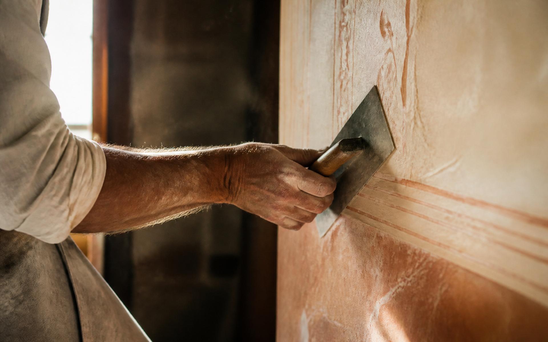 Le mani di un artigiano al lavoro su una parete a base calce